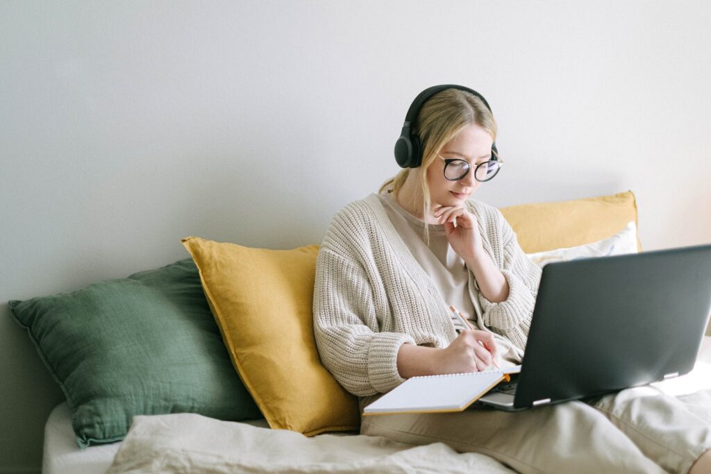 Eine junge Frau sitzt auf dem Bett mit einem Laptop auf dem Schoß und lernt mit MOOCs